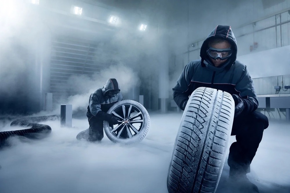 Mechaniker hält einen Winterreifen in einer dunstigen Werkstatt, Jaguar Land Rover Winterräder und -reifen