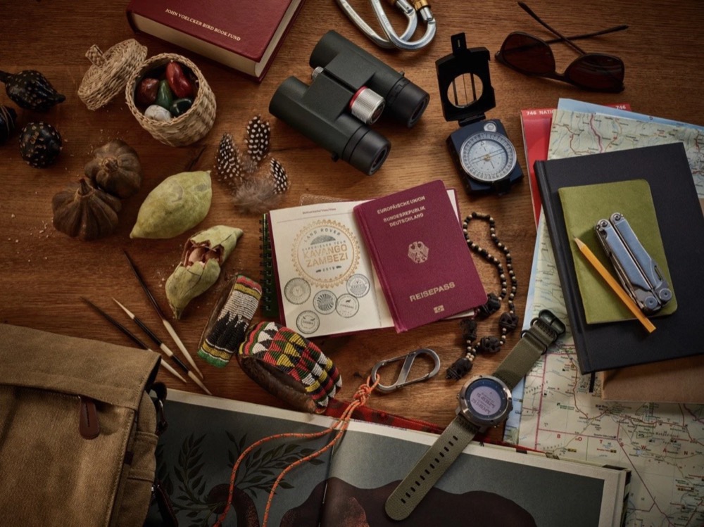 Reise-Flatlay mit Reisepass, Fernglas, Kompass, Karten und Notizbuch für die Land Rover Experience Tour