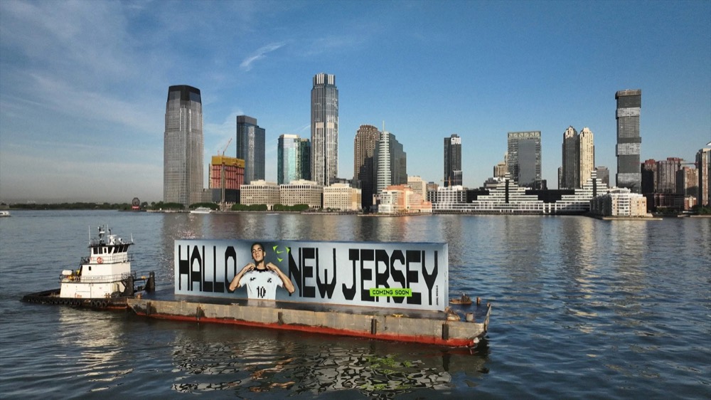 Schlepper schiebt die „Hallo New Jersey“-Werbebarge an der Skyline von Jersey City vorbei, Nike Football Jamal Musiala WM 2026