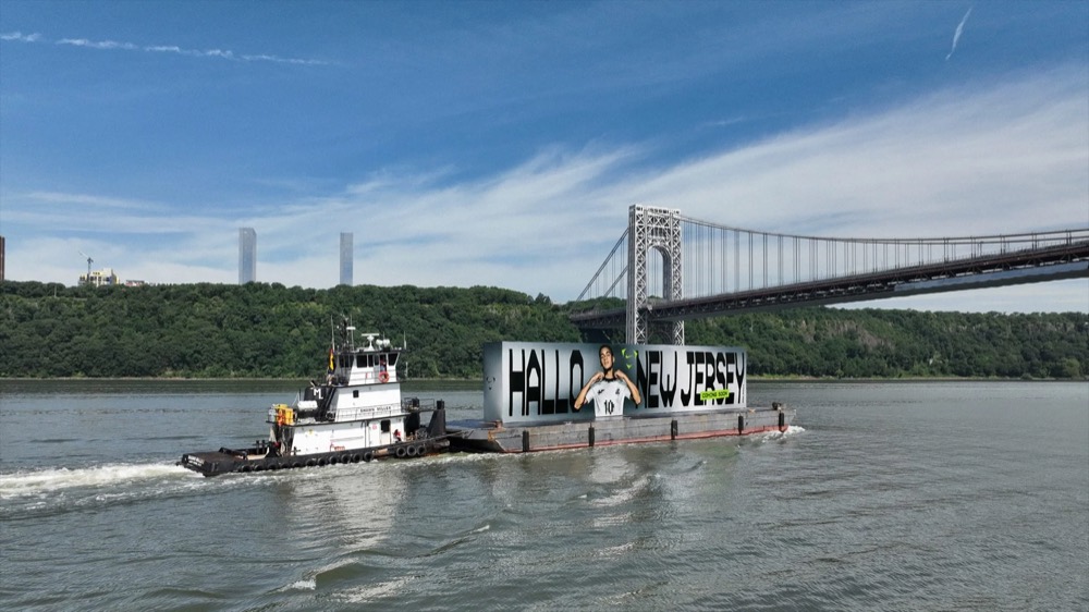 Schlepper schiebt die „Hallo New Jersey“-Werbebarge an der George Washington Bridge vorbei, Nike Football Jamal Musiala WM 2026