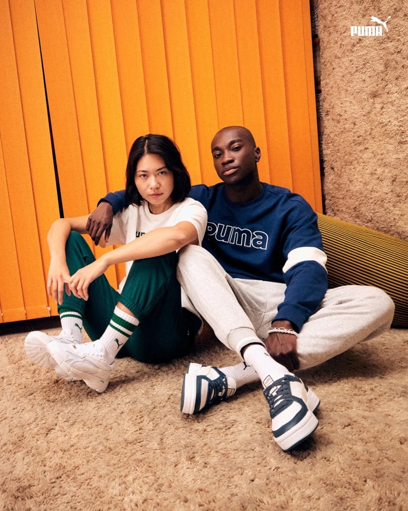 Zwei Models in Puma-Outfits sitzen vor einer orangefarbenen Wand, Puma AW23