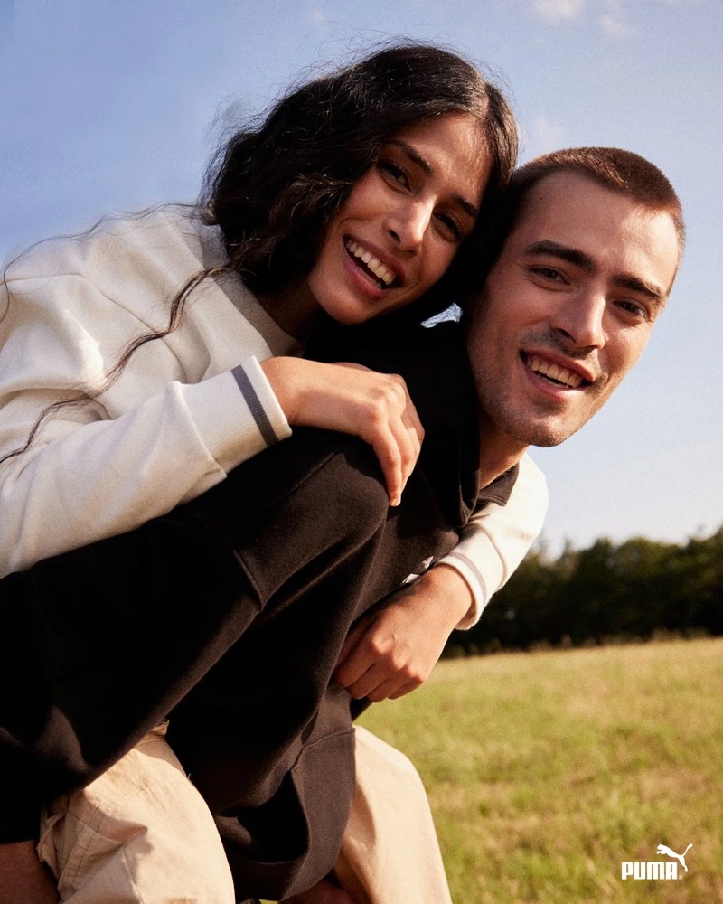 Paar lächelt auf einem Feld in die Kamera, Puma AW23