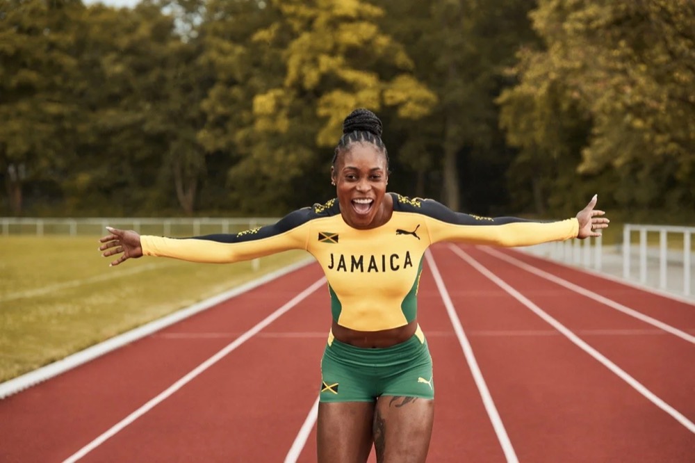 Elaine Thompson-Herah im Jamaika-Trikot mit ausgebreiteten Armen auf einer Laufbahn, Puma