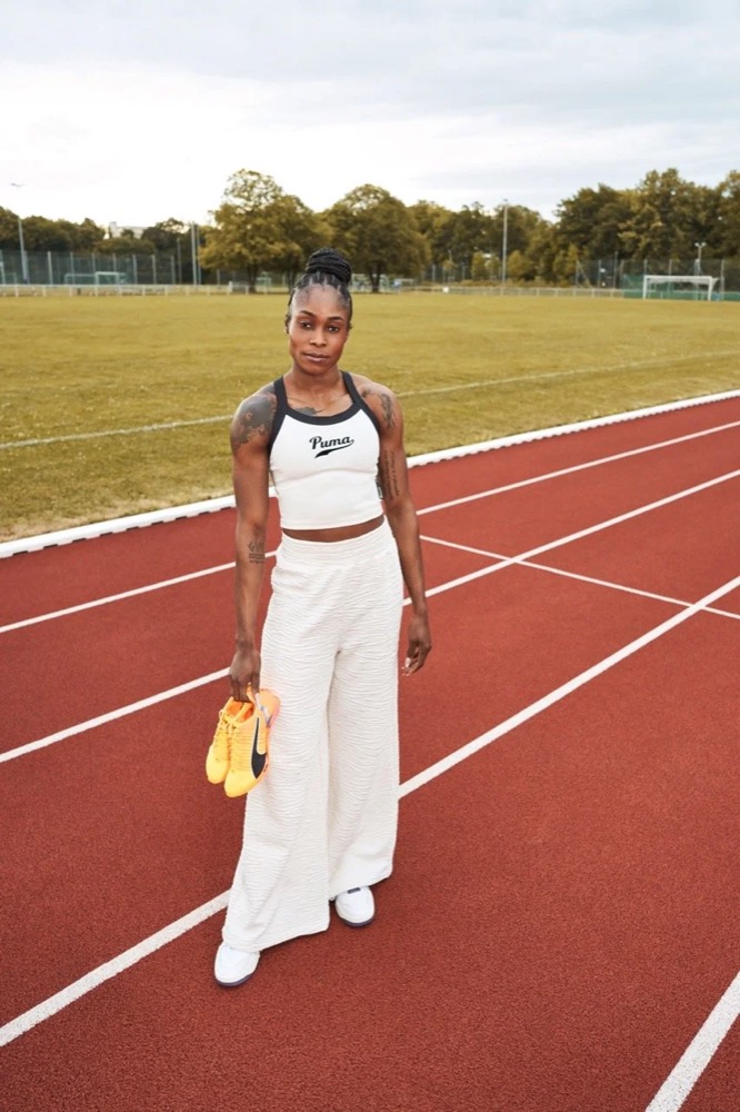 Elaine Thompson-Herah im weißen Outfit mit orangefarbenen Puma-Spikes auf der Laufbahn