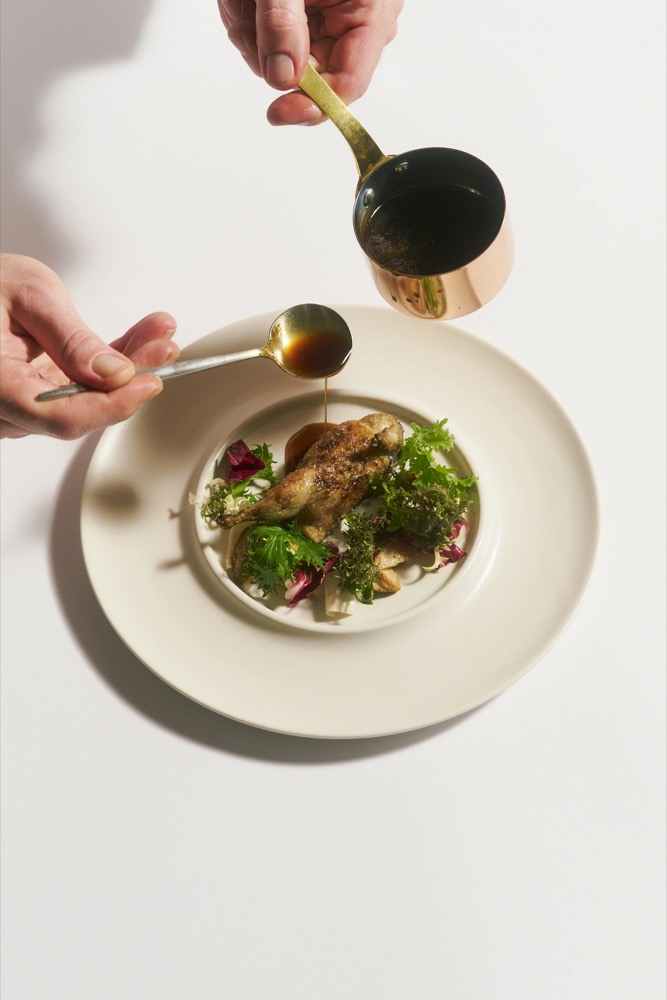 Sauce wird aus einem Kupfertopf über einen Hauptgang gegossen, Foodfotografie für das Restaurant Rausch