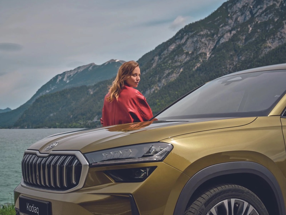 Frau neben einem Škoda Kodiaq auf einer Bergstraße, Škoda-Zubehörkampagne