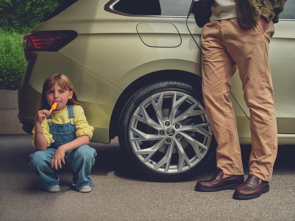 Kind sitzt neben einem Škoda Superb, ein Mann steht daneben, Škoda-Zubehörkampagne
