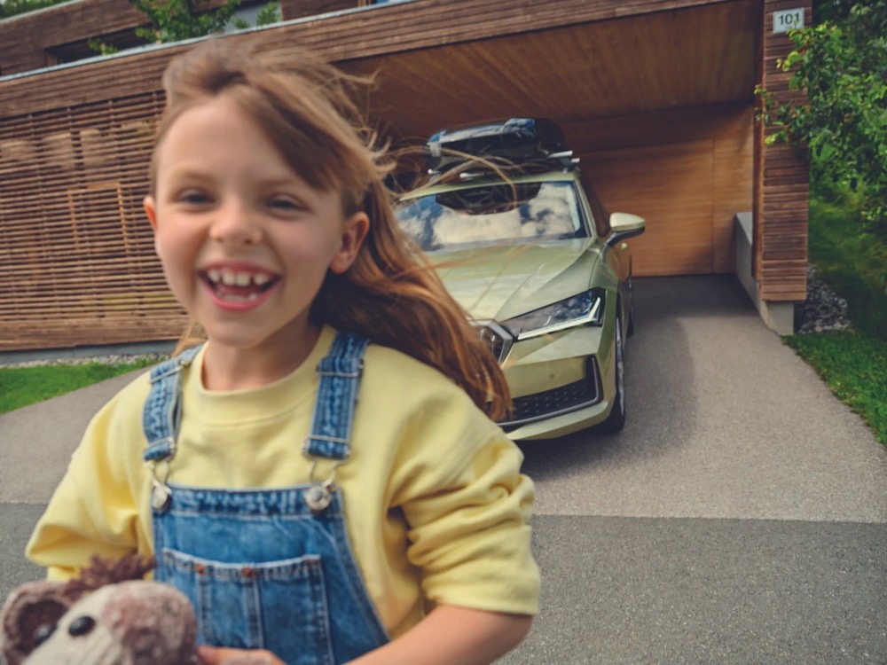 Lächelndes Mädchen in Latzhose vor einem Škoda Superb, Škoda-Zubehörkampagne