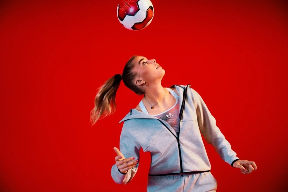 Laura Freigang köpft einen Fußball in einem roten Studio, Under Armour