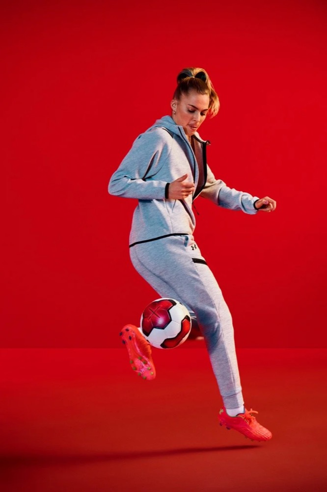 Laura Freigang läuft im Under-Armour-Trainingsanzug vor rotem Hintergrund