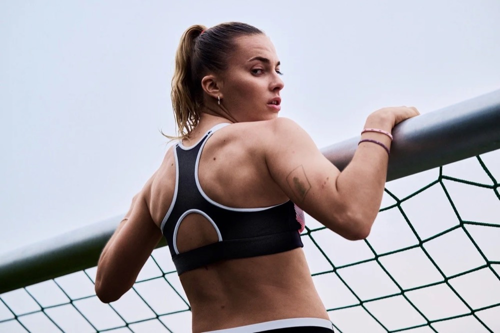Laura Freigang im Under-Armour-Sport-BH an einem Fußballnetz, Rückansicht